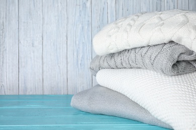 Image of Stack of folded warm sweaters on turquoise wooden table. Space for text