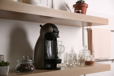 Photo of Modern coffeemaker with glass cup on wooden shelf