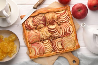 Photo of Tasty fresh apple galette, ingredients and knife on white wooden table, flat lay