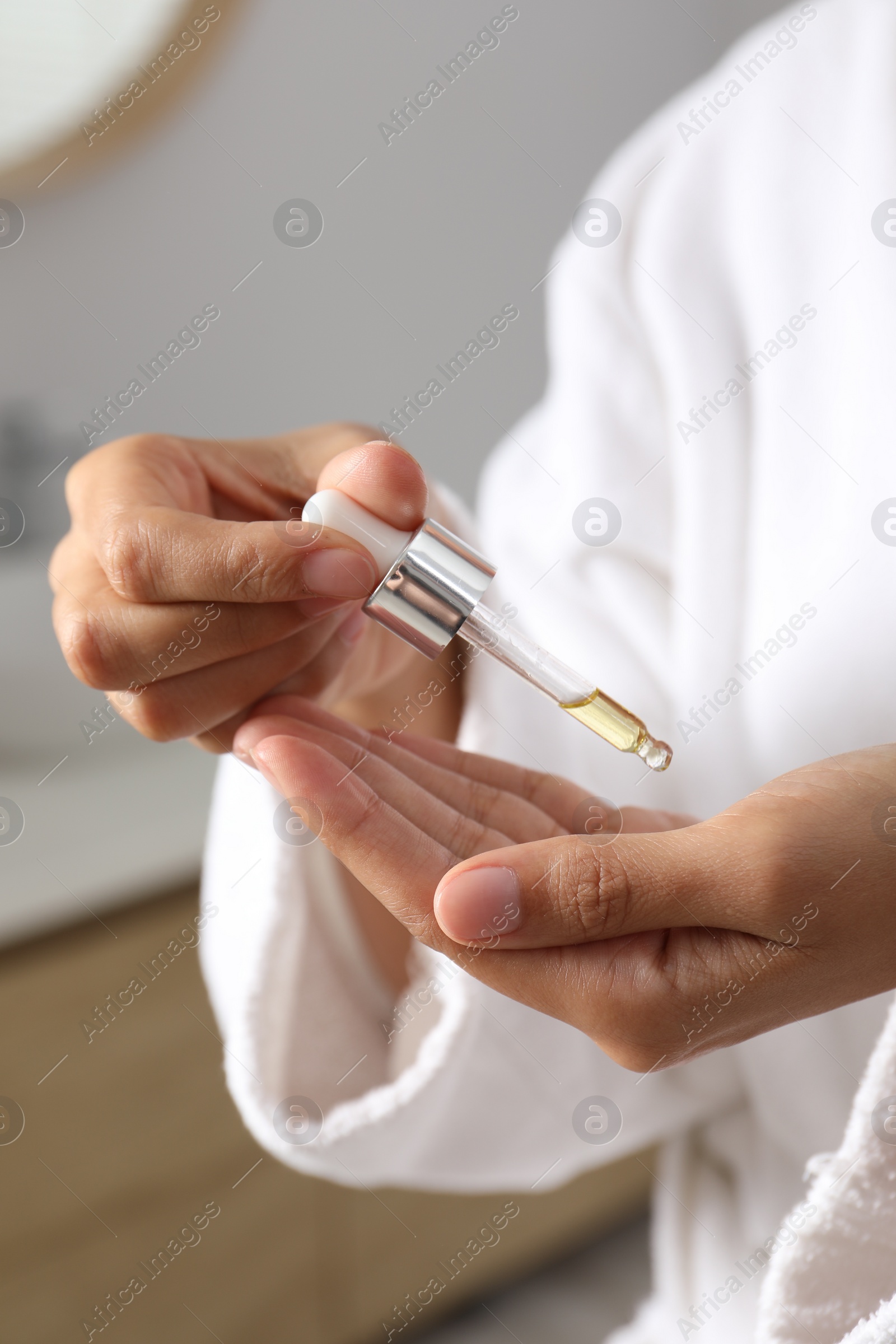 Photo of Woman applying cosmetic serum onto her hand on blurred background, closeup