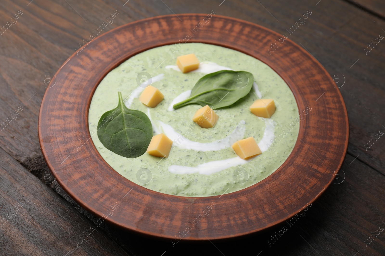 Photo of Delicious spinach cream soup with leaves and cheese in bowl on wooden table, closeup