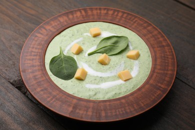 Photo of Delicious spinach cream soup with leaves and cheese in bowl on wooden table, closeup