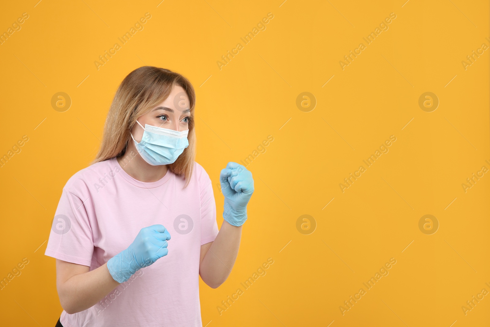Photo of Woman with protective mask and gloves in fighting pose on yellow background. Strong immunity concept
