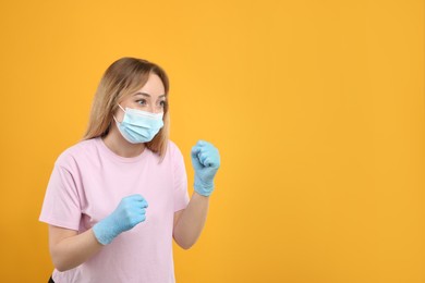 Woman with protective mask and gloves in fighting pose on yellow background. Strong immunity concept