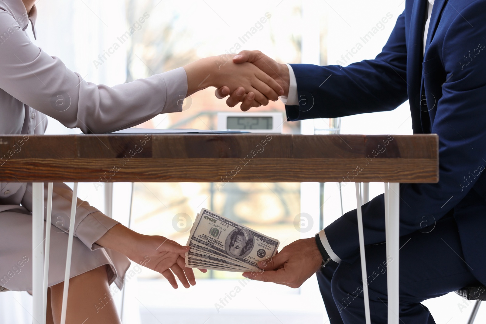Photo of Man shaking woman's hand and giving bribe money under table, closeup