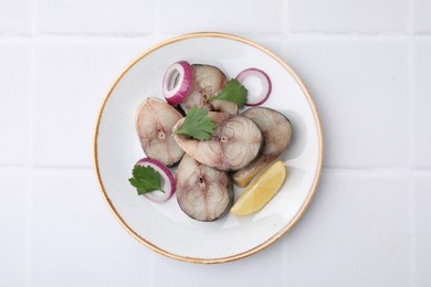 Photo of Slices of tasty salted mackerel with lemon and onion on white tiled table, top view