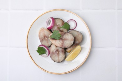 Slices of tasty salted mackerel with lemon and onion on white tiled table, top view