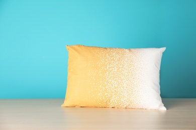 Soft decorative pillow on table against color background