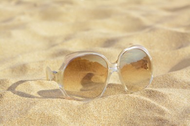Photo of Stylish sunglasses with light brown lenses on sandy beach, closeup