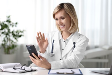 Photo of Smiling doctor with smartphone having online consultation at table in office