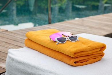 Photo of Beach towels and sunglasses on sun lounger near outdoor swimming pool