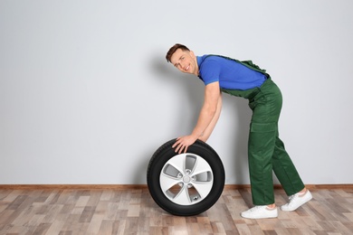 Male mechanic with car tire on light wall background