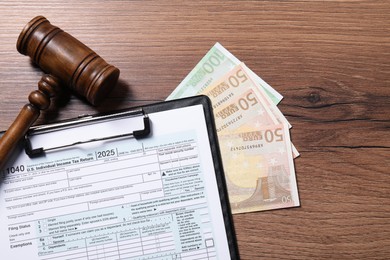 Tax return form, euro banknotes and gavel on wooden table, top view