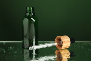 Photo of Bottle of face serum and dropper on wet surface against green background, closeup