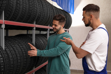 Mechanic helping client to choose car tire in auto store