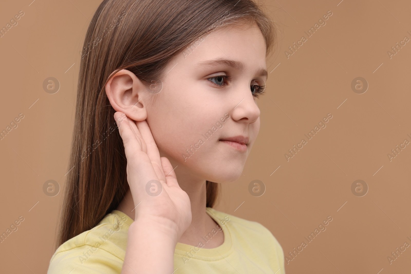 Photo of Little girl with hearing problem on pale brown background, space for text