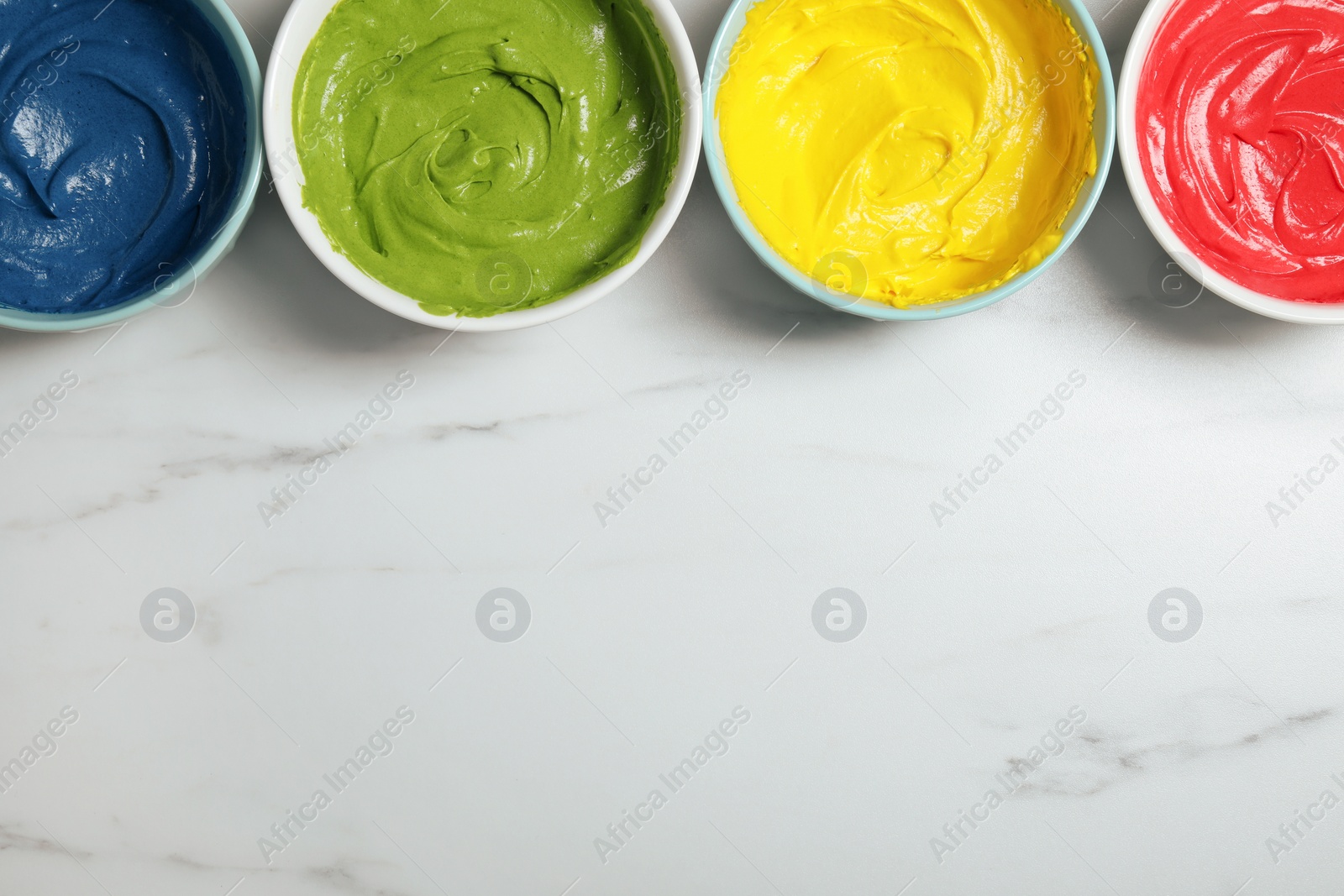 Photo of Bowls of different cream with food coloring on white marble table, flat lay. Space for text