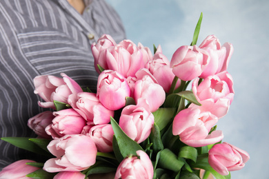 Woman with beautiful pink spring tulips on light blue background, closeup