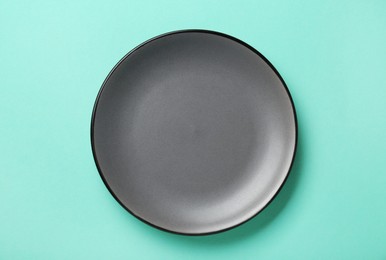 Photo of Empty grey ceramic plate on turquoise background, top view