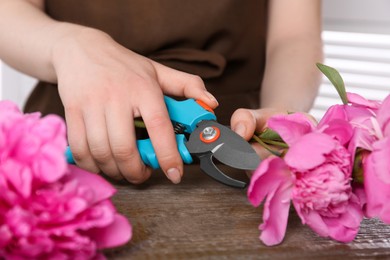 Woman trimming beautiful pink peonies with secateurs at wooden table, closeup