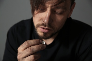 Young addicted man with drugs on grey background