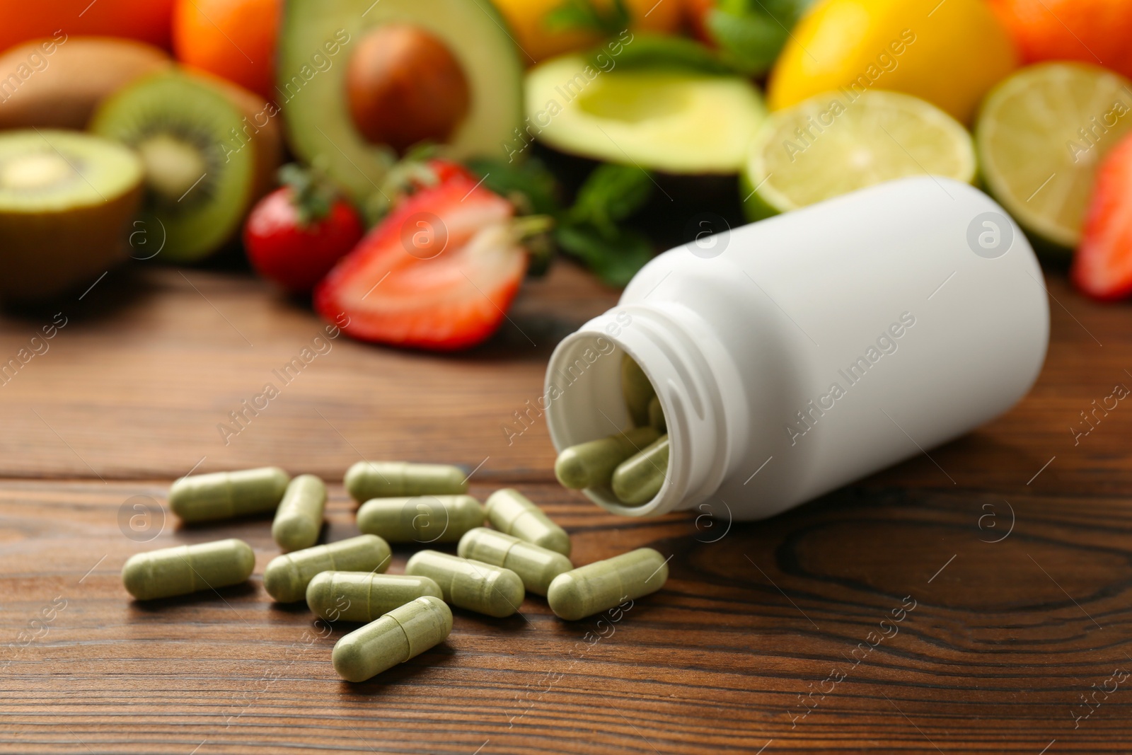 Photo of Vitamin pills, bottle and fresh fruits on wooden table