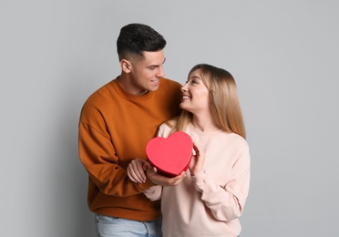 Photo of Man surprising his girlfriend with gift on grey background. Valentine's day celebration