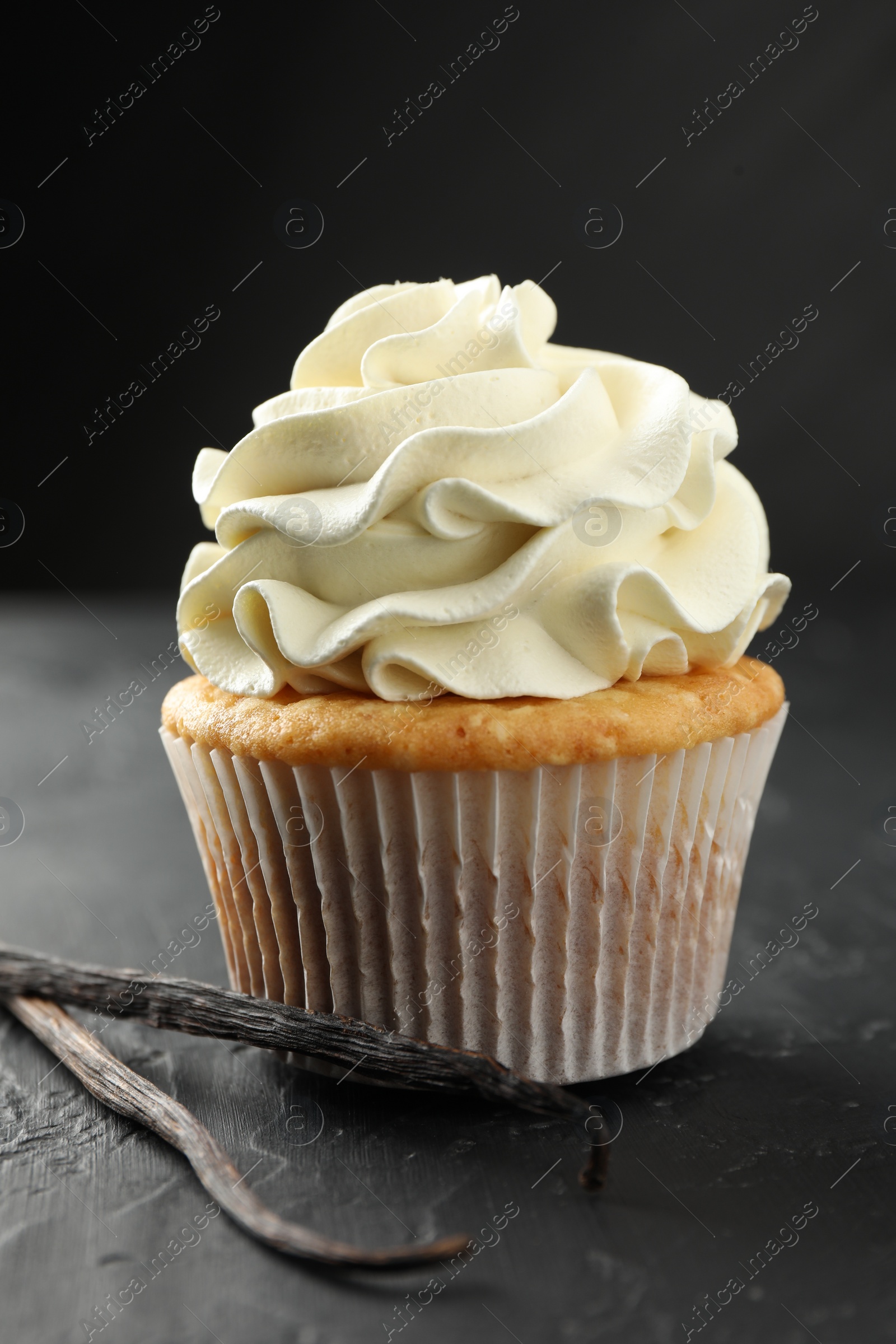 Photo of Tasty cupcake with cream and vanilla pods on black table, closeup