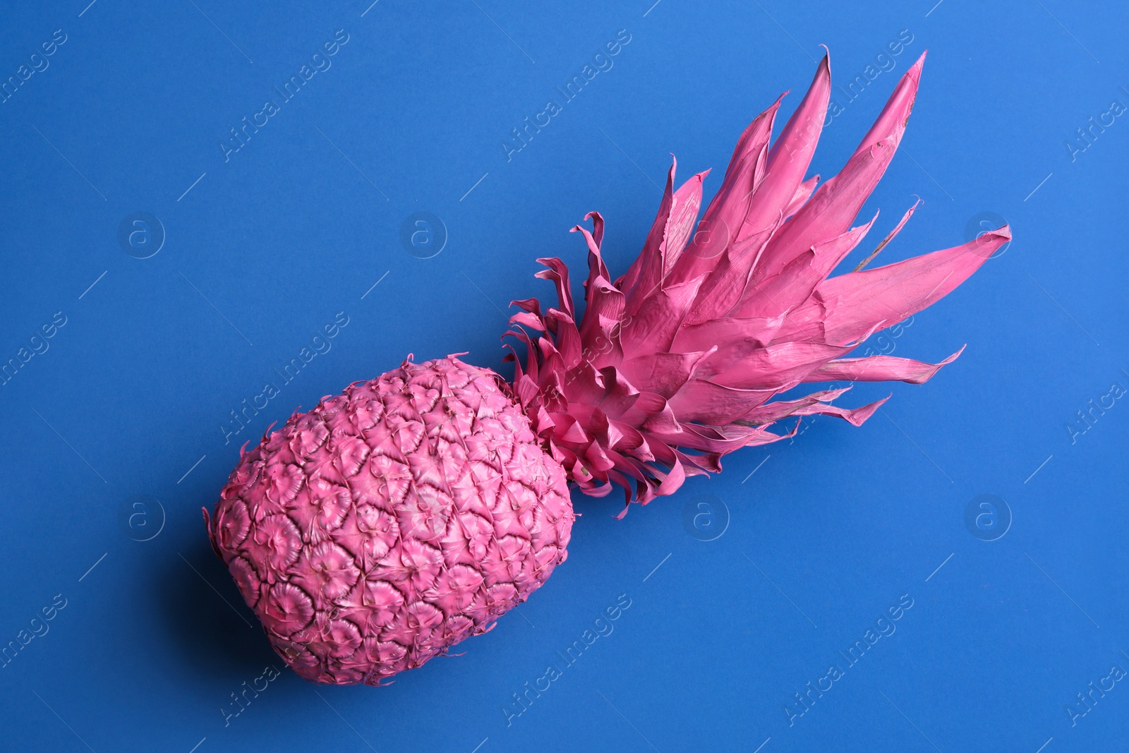 Photo of Pink pineapple on blue background, top view. Creative concept