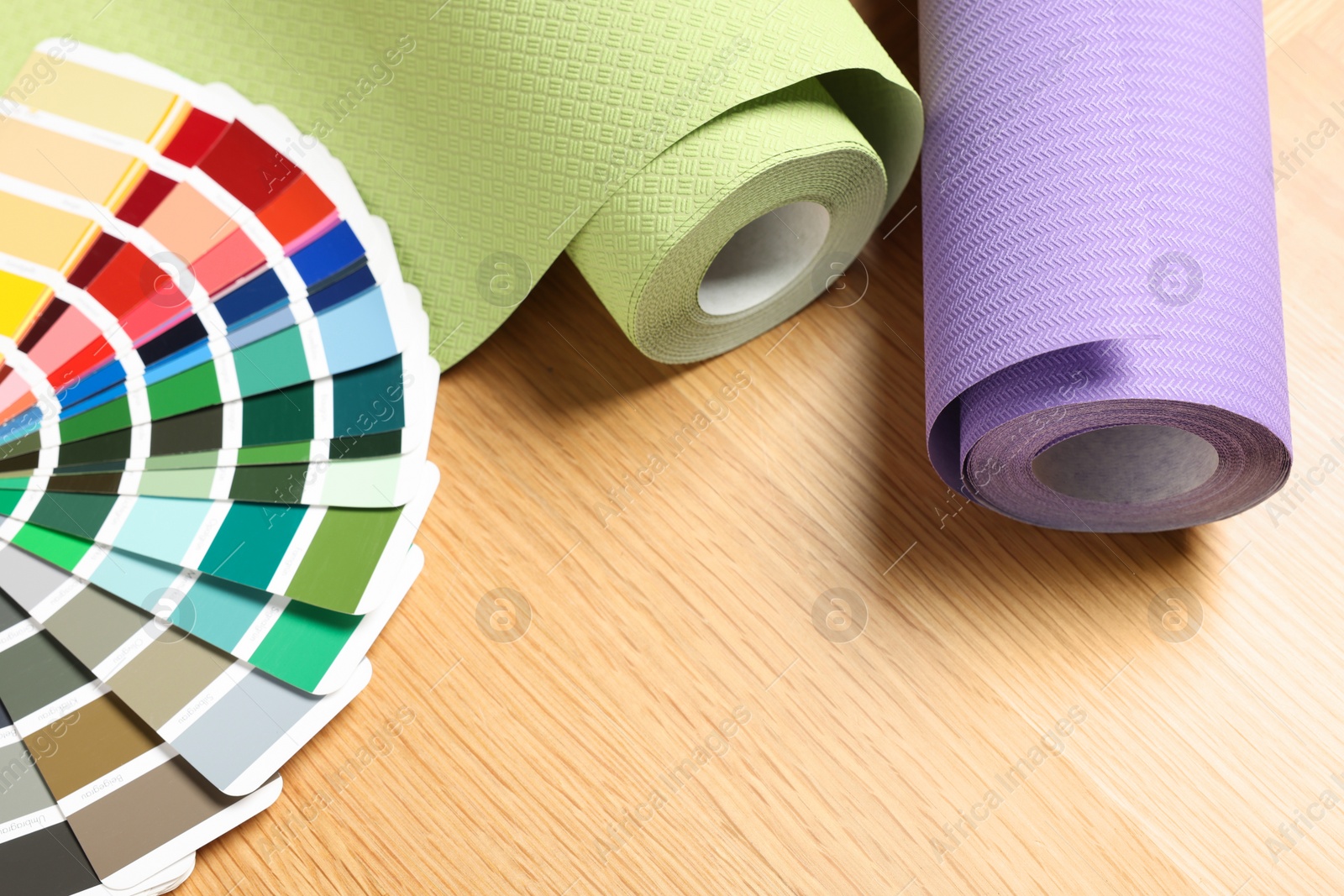 Photo of Different wallpaper rolls and color palette samples on wooden table, space for text