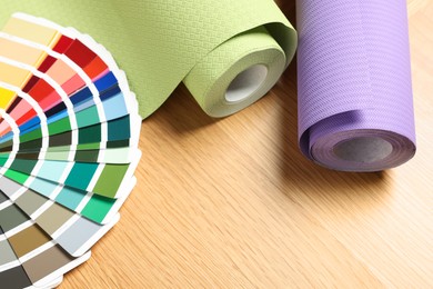 Photo of Different wallpaper rolls and color palette samples on wooden table, space for text