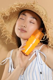 Photo of Beautiful young woman in straw hat holding sun protection cream on beige background