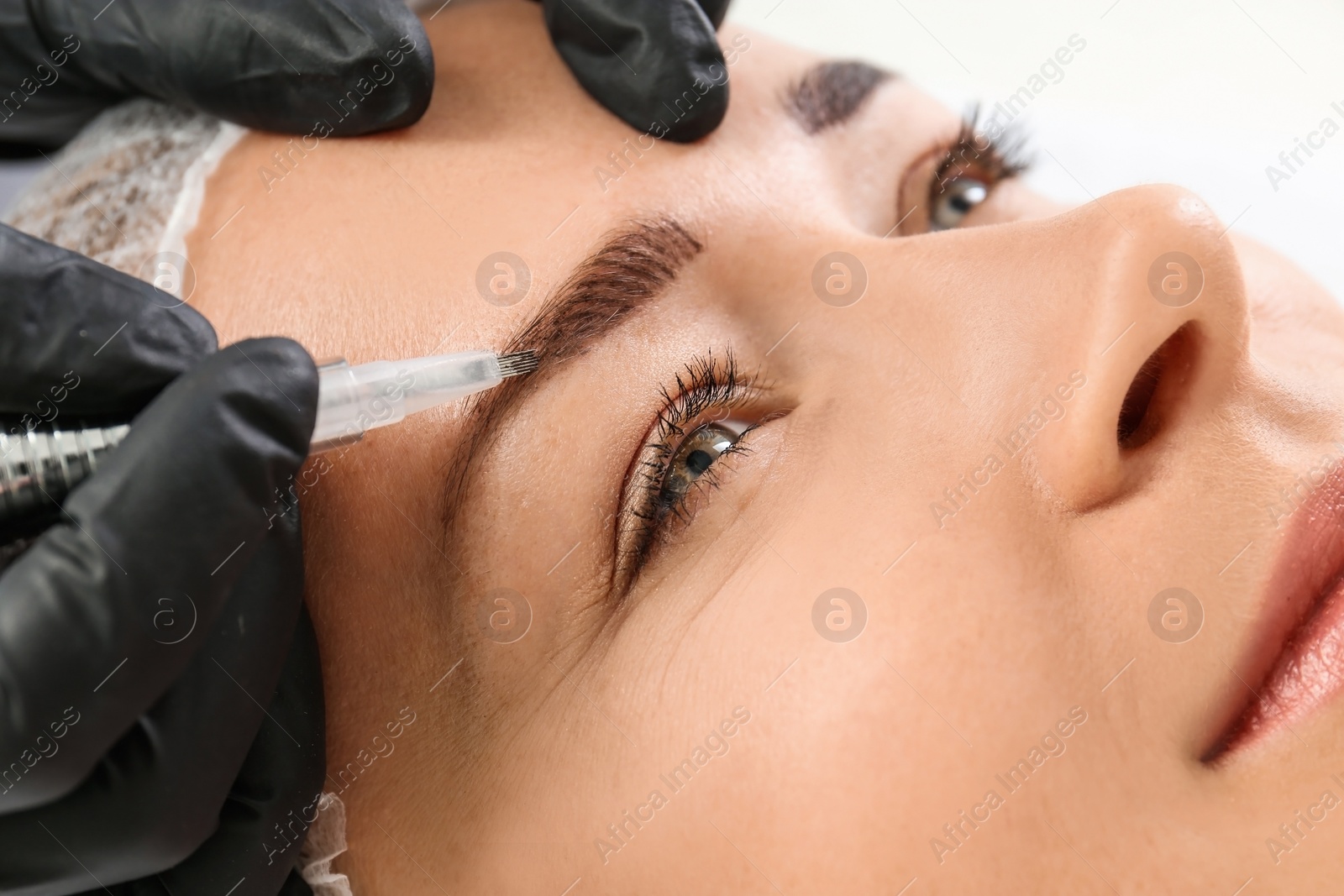 Photo of Young woman undergoing eyebrow correction procedure in salon