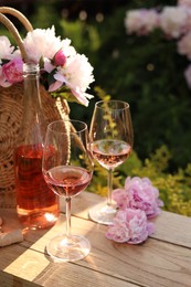 Photo of Bottle and glasses of rose wine near beautiful peonies on wooden table in garden