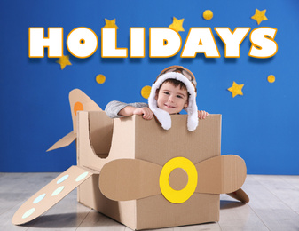 School holidays. Cute little child playing with cardboard plane near blue wall