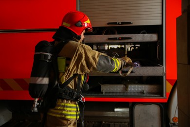 Photo of Firefighter in uniform with safety equipment near fire truck at station