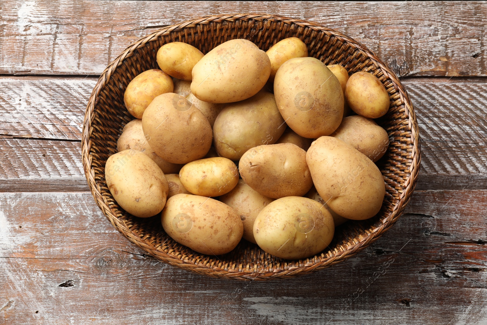 Photo of Raw fresh potatoes in wicker basket on wooden table, top view