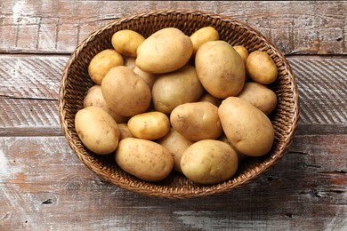 Photo of Raw fresh potatoes in wicker basket on wooden table, top view