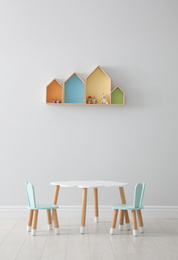 Photo of House shaped shelves and little table with chairs in children's room. Interior design