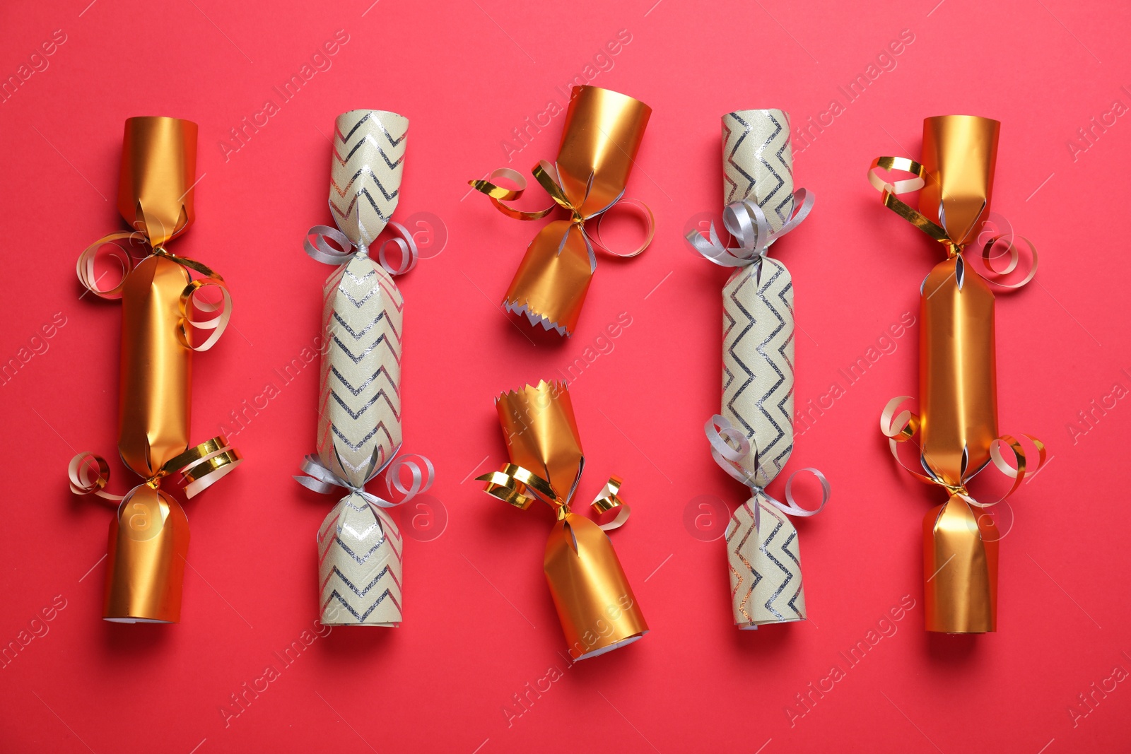 Photo of Bright Christmas crackers on red background, flat lay