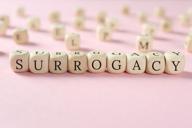 Word Surrogacy made of wooden cubes on pink background, closeup