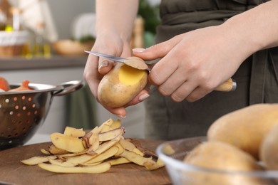 Woman peeling fresh potato with knife at table indoors, closeup