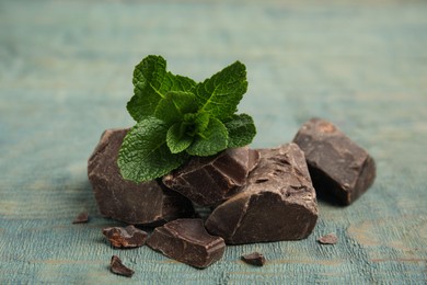 Photo of Tasty dark chocolate pieces with mint on blue wooden table