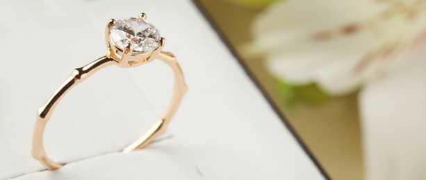 Image of Beautiful engagement ring in box against blurred background, closeup view with space for text. Banner design