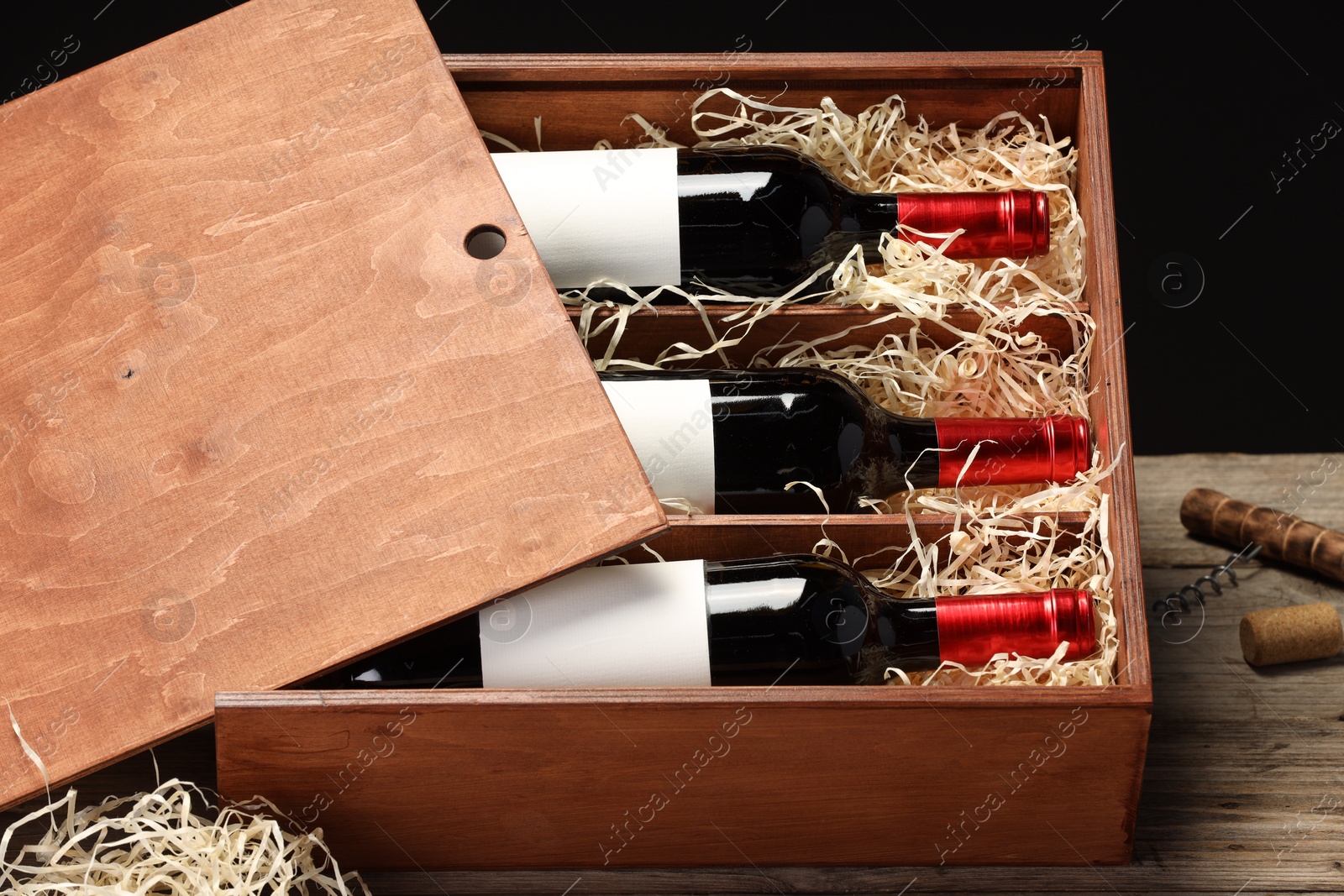 Photo of Box with wine bottles on wooden table against black background