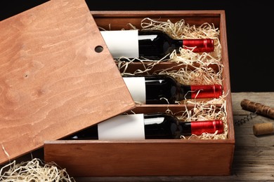 Box with wine bottles on wooden table against black background