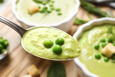 Spoon with fresh vegetable detox soup made of green peas on blurred background, closeup