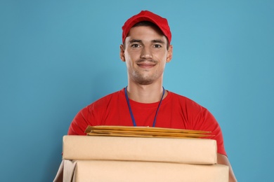 Happy young courier with parcels and envelopes on blue background