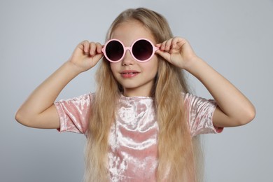 Girl in stylish sunglasses on light grey background