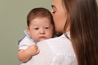 Photo of Mother kissing her cute newborn baby on olive background